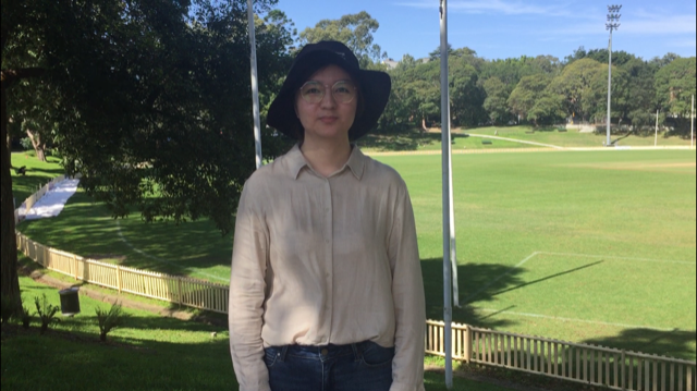 Jiani stands in the shade with a university oval in the background